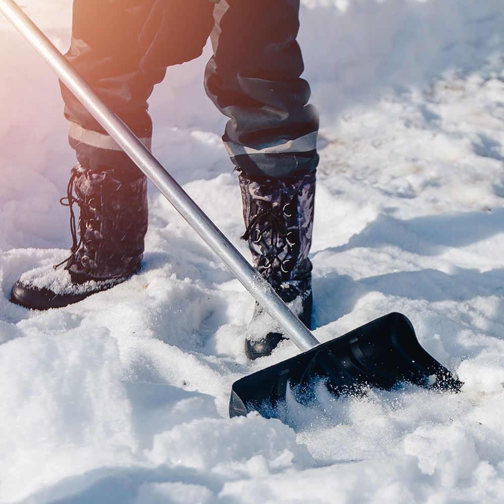 Person beim Schneeschaufeln mit einer schwarzen Schaufel