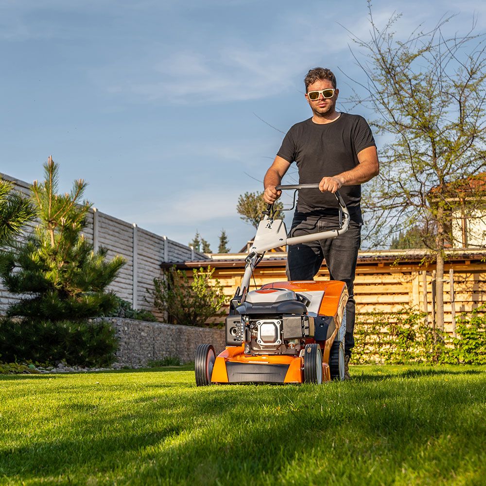 Eine Person, die bei schönem Wetter mit einem Rasenmäher einen grünen Rasen mäht.